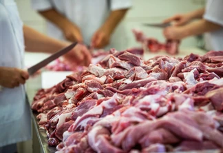 A foto mostra em primeiro plano pedaços de carne sobre superfície. No fundo, pessoas seguram facas e cortam. A foto mostra em primeiro plano pedaços de carne sobre superfície. No fundo, pessoas seguram facas e cortam.