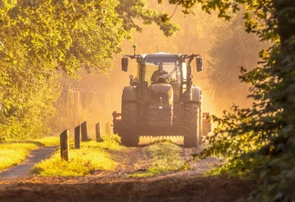Trator na luz dourada e nebulosa do nascer do sol. Veículo agrícola em estrada de terra pela manhã. Trator na luz dourada e nebulosa do nascer do sol. Veículo agrícola em estrada de terra pela manhã.
