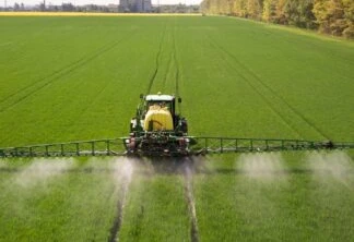 Trator pulverizando pesticidas químicos com pulverizador em grande lavoura agrícola verde.