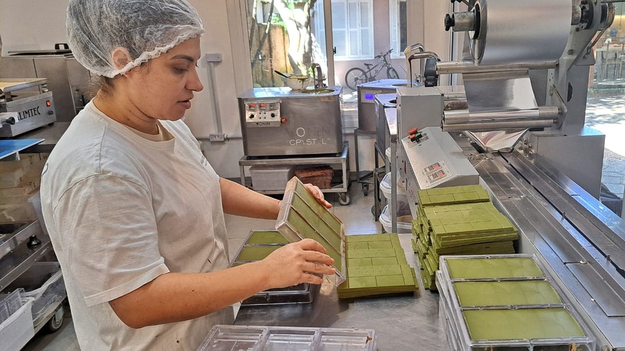 Foto de mulher com EPI em fábrica realizando a produção de chocolate branco com erva-mate. Foto de mulher com EPI em fábrica realizando a produção de chocolate branco com erva-mate.