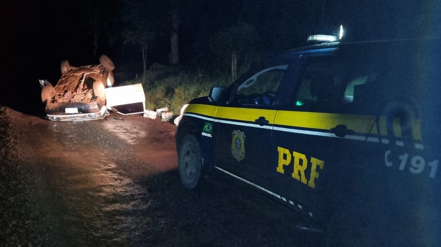 Foto viatura da PRF próxima a carro capotado com galões de agrotóxicos caídos no chão. Foto viatura da PRF próxima a carro capotado com galões de agrotóxicos caídos no chão.