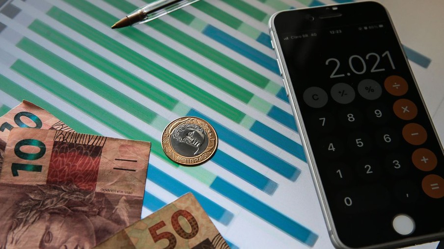 Foto de celular, notas e moedas de real sobre gráfico. Foto de celular, notas e moedas de real sobre gráfico.