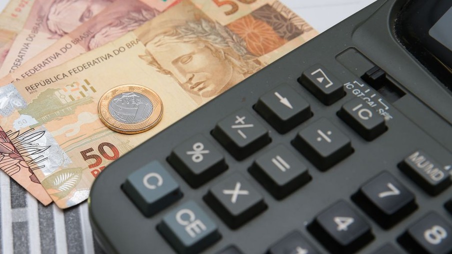 Foto de notas de real e uma moeda ao lado de calculadora. Foto de notas de real e uma moeda ao lado de calculadora.