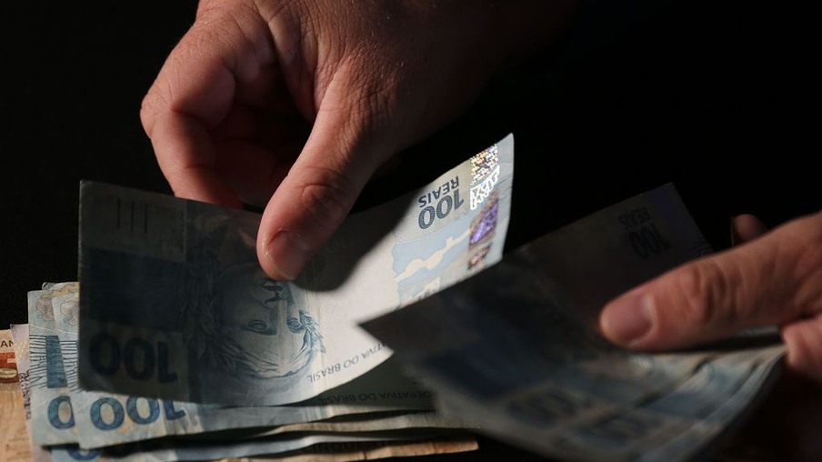 Foto de mãos contando notas de real. Foto de mãos contando notas de real.