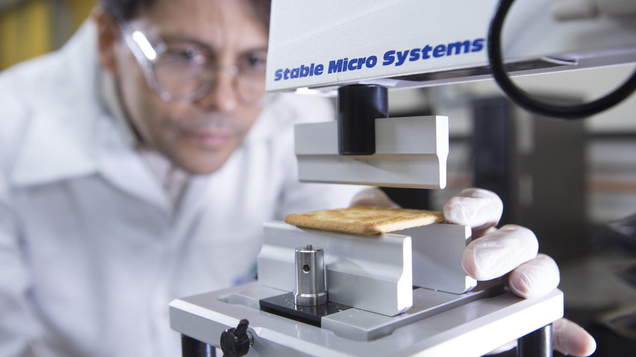 Foto de pesquisador realizando análise de textura dos extrudados. Foto de pesquisador realizando análise de textura dos extrudados.