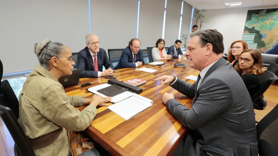Foto com a ministra Marina Silva sentada na ponta de uma mesa de reuniões. Ao lado dela está o ministro Carlos Fávaro e outras pessoas estão sentadas ao redor da mesa.