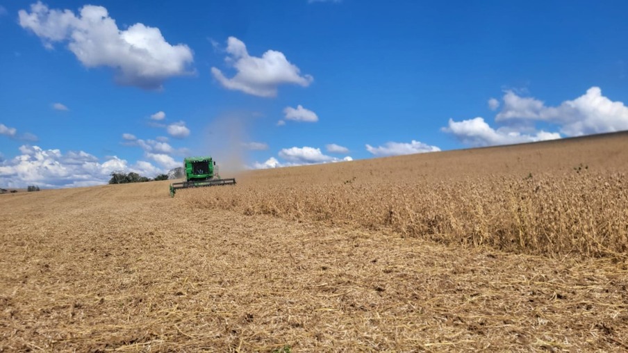 Foto de colheitadeira operando em lavoura de soja sob céu azul com poucas nuvens. Foto de colheitadeira operando em lavoura de soja sob céu azul com poucas nuvens.