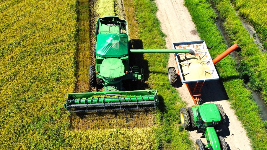 Foto de colheitadeira em lavoura de arroz despejando grãos em carreta graneleira. Foto de colheitadeira em lavoura de arroz despejando grãos em carreta graneleira.