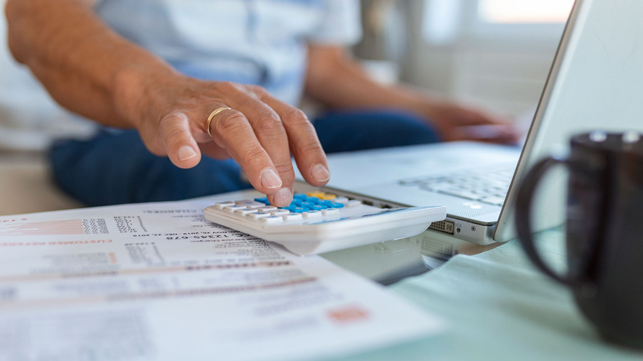 Foto focada em mãos de homem mexendo em calculadora. Foto focada em mãos de homem mexendo em calculadora.