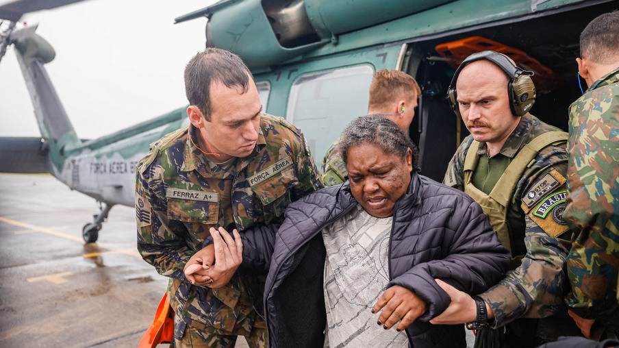 Foto de mulher saindo de helicóptero sendo amparada por militares. Foto de mulher saindo de helicóptero sendo amparada por militares.