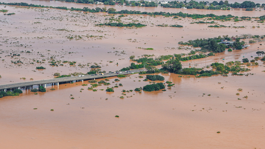 Foto de área e rodovia submersas em água com tom marrom. Foto de área e rodovia submersas em água com tom marrom.