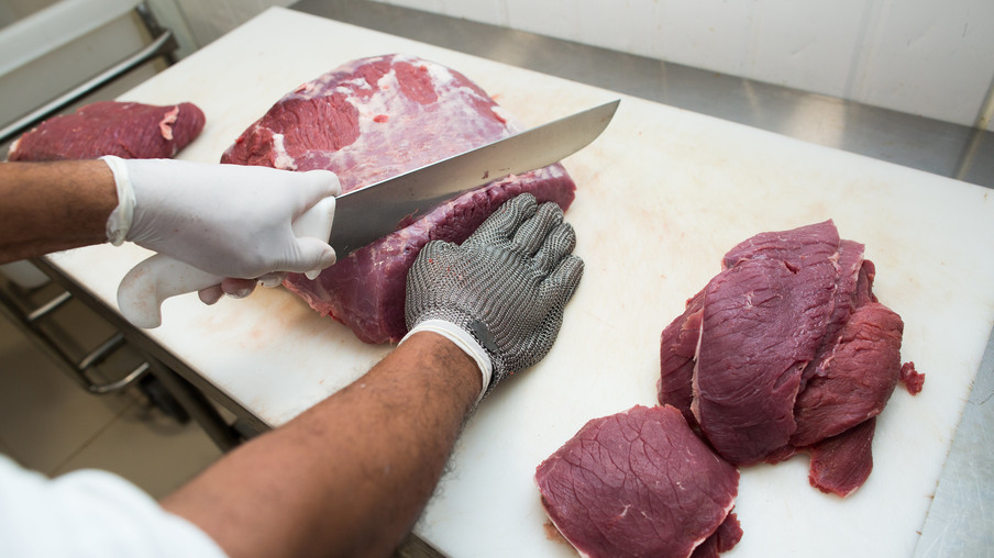 Foto focada em mãos com luvas cortando carne com faca. Foto focada em mãos com luvas cortando carne com faca.