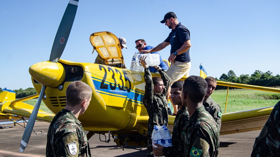 Foto de um grupo de militares alcançando água para dois homens estão colocando as garrafas em um avião agrícola amarelo. Foto de um grupo de militares alcançando água para dois homens estão colocando as garrafas em um avião agrícola amarelo.