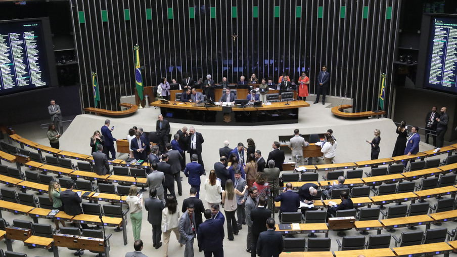 Foto do plenário do Congresso Nacional com políticos sentados à mesa da presidência e os demais em pé na frente do plenário. Foto do plenário do Congresso Nacional com políticos sentados à mesa da presidência e os demais em pé na frente do plenário.