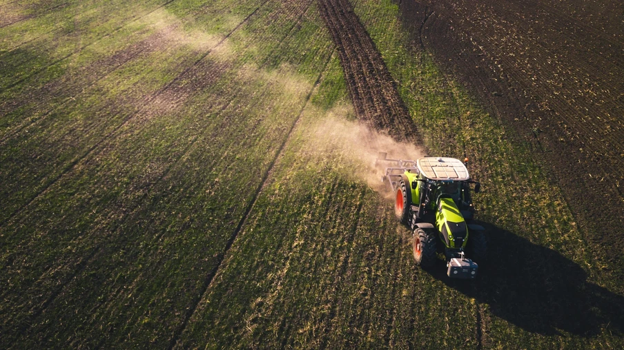 A foto é aérea e mostra um trator em meio a uma grande área de terra. A foto é aérea e mostra um trator em meio a uma grande área de terra.