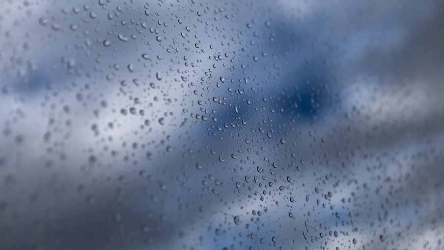 Foto de gotas de água em vidro. Ao fundo, aparece o céu com nuvens escuras. Foto de gotas de água em vidro. Ao fundo, aparece o céu com nuvens escuras.