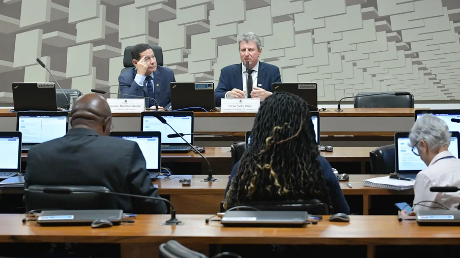 A foto mostra pessoas em uma sala do Senado, três delas estão de costas olhando para a mesa, onde estão o presidente da Empresa Brasileira de Pesquisas Agropecuárias (Embrapa) em exercício, Clênio Nailto Pillon, em pronunciamento, e o senador Hamilton Mourão. A foto mostra pessoas em uma sala do Senado, três delas estão de costas olhando para a mesa, onde estão o presidente da Empresa Brasileira de Pesquisas Agropecuárias (Embrapa) em exercício, Clênio Nailto Pillon, em pronunciamento, e o senador Hamilton Mourão.