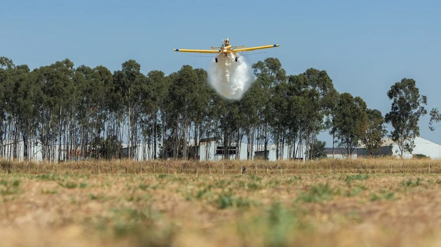 Foto de avião agrícola amarelo dispersando produtos sobre área agrícola. Foto de avião agrícola amarelo dispersando produtos sobre área agrícola.