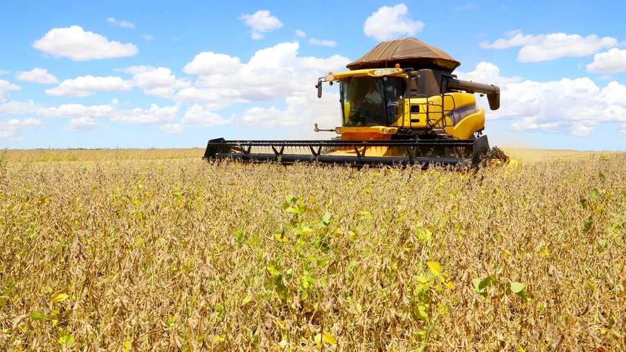 Foto de colheitadeira amarela avançando em lavoura de soja. Foto de colheitadeira amarela avançando em lavoura de soja.