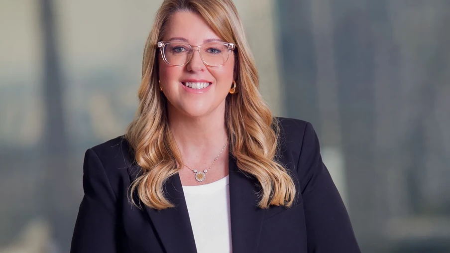 Foto de mulher branca, com cabelo loiro comprido e óculos sorrindo. Ele usa blusa branca, colar prata e blazer escuro. Foto de mulher branca, com cabelo loiro comprido e óculos sorrindo. Ele usa blusa branca, colar prata e blazer escuro.