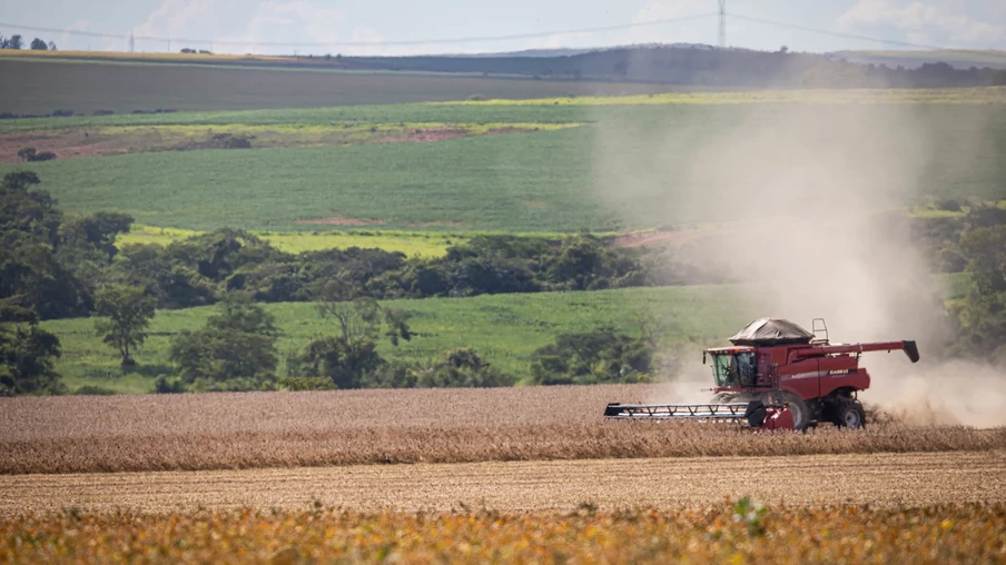 A foto mostra uma colheitadeira vermelha avançando em lavoura de soja. A foto mostra uma colheitadeira vermelha avançando em lavoura de soja.