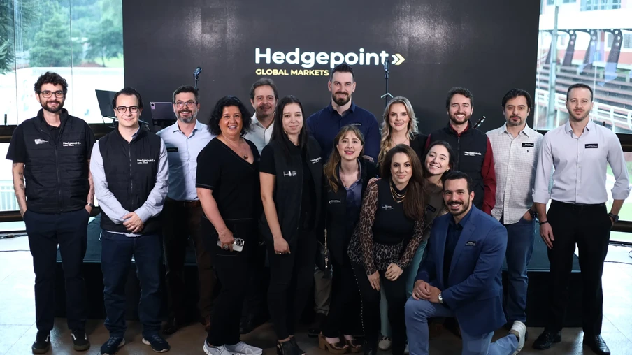 Foto de pessoas posando para foto em frente a letreiro com a logo da Hedgepoint Global Markets. Elas estão sorrindo para foto e a maioria usa roupas escuras. Foto de pessoas posando para foto em frente a letreiro com a logo da Hedgepoint Global Markets. Elas estão sorrindo para foto e a maioria usa roupas escuras.
