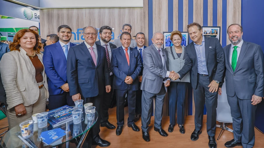 Foto de vários homens e duas mulheres lado a lado sorrindo. O presidente Lula está no centro e cumprimenta um dos homens. Foto de vários homens e duas mulheres lado a lado sorrindo. O presidente Lula está no centro e cumprimenta um dos homens.