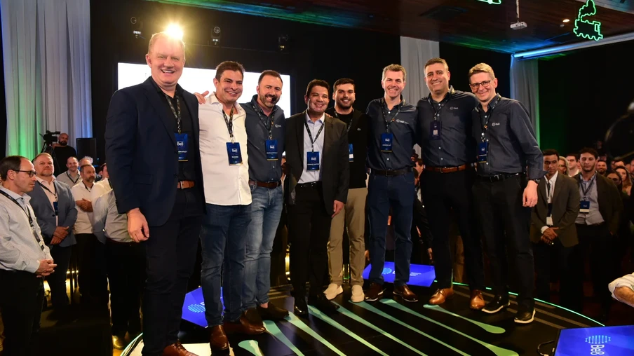 Foto com oito homens, lado a lado, com roupas formais durante evento. Eles sorriem para a foto. Foto com oito homens, lado a lado, com roupas formais durante evento. Eles sorriem para a foto.