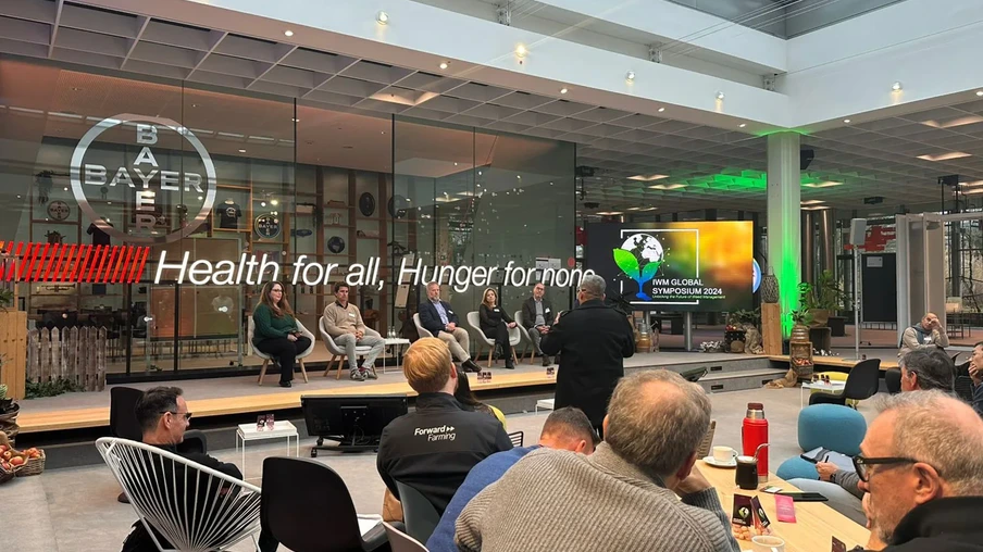 Foto de pessoas sentadas ao redor de mesas assistindo a painel com cinco pessoas sentadas ao lado e um telão. Foto de pessoas sentadas ao redor de mesas assistindo a painel com cinco pessoas sentadas ao lado e um telão.