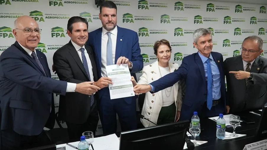 Foto de cinco parlamentares homens e uma mulher segurando documento enquanto sorriem para foto. No fundo está um painel da FPA. Foto de cinco parlamentares homens e uma mulher segurando documento enquanto sorriem para foto. No fundo está um painel da FPA.