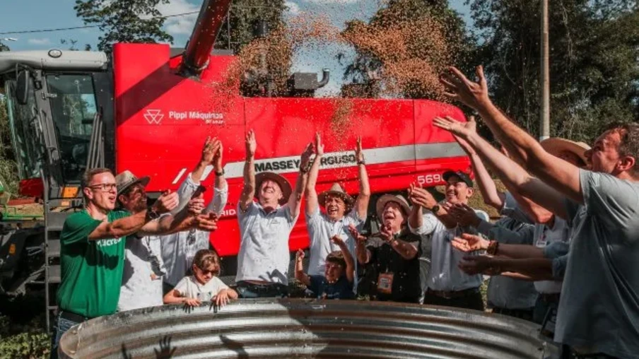 Foto de pessoas ao redor de tonel com grãos de soja caindo. Atrás deles está uma máquina agrícola vermelha. Foto de pessoas ao redor de tonel com grãos de soja caindo. Atrás deles está uma máquina agrícola vermelha.