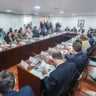 Foto de Reunião na sala de situação sobre as chuvas no Rio Grande do Sul, no Palácio do Planalto. Muitas pessoas estão sentadas ao redor de mesa enquanto conversam e analisam papéis.